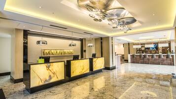 Un moderno vestíbulo de hotel con mostradores de recepción de mármol, una zona de bar y un techo con una lámpara de diseño único.