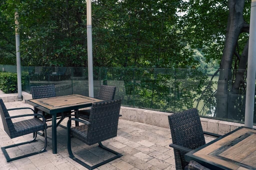 Eine Terrassenanlage im Freien mit Tisch und Stühlen, umgeben von einem Glasgeländer und viel Grün.