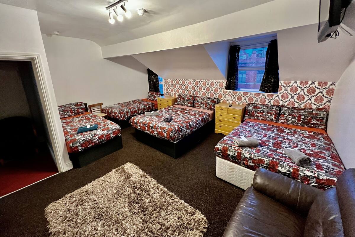 A bedroom with four beds, a brown leather sofa, a small rug, and a window with patterned curtains.