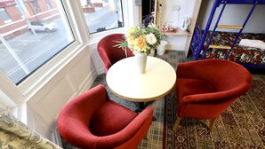 A room with a round table, two red chairs, a vase with flowers, a bunk bed, and a window with a view of the street. - Blackpool Central Hotel (Blackpool)