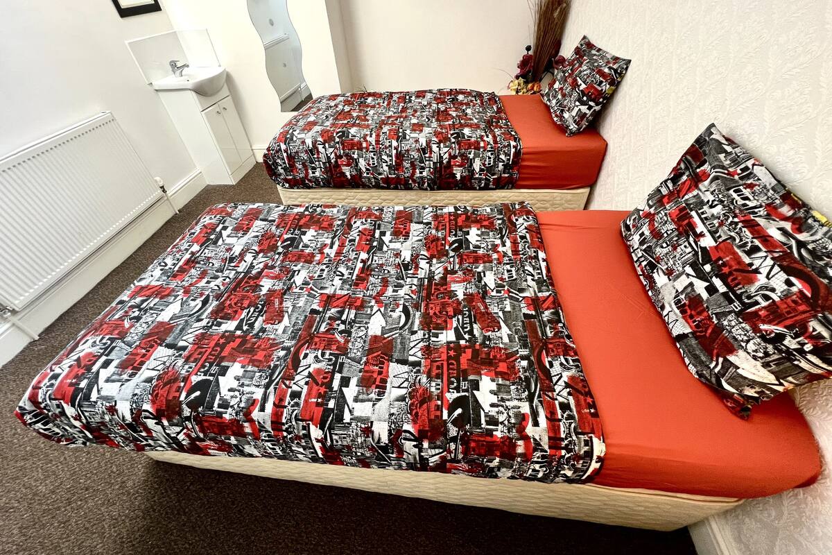 A bedroom with two beds, each with red bedding and a patterned duvet cover.