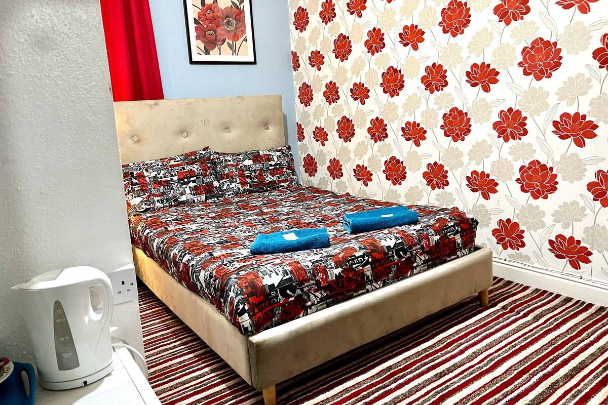 A bedroom with a bed, a kettle, and a patterned carpet.