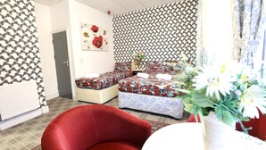 A room with patterned wallpaper, a bed with floral bedding, a red chair, and a vase with flowers. - Blackpool Central Hotel (Blackpool)