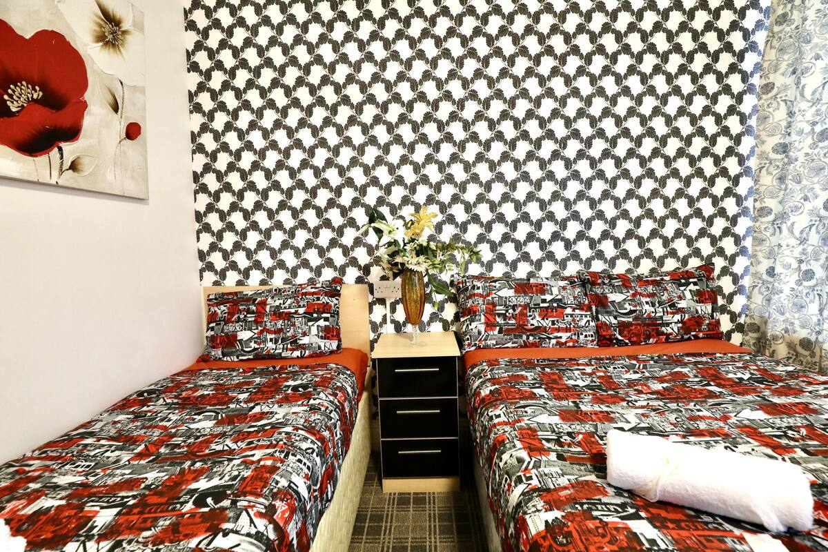 A bedroom with two beds, a nightstand, and a vase with flowers.