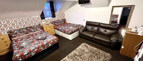A bedroom with a bed, a sofa, a TV, and a mirror.