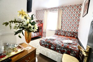 Un dormitorio con cama, mesita de noche con un florero, una silla y cómoda.