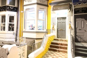 Entrada de hotel con suelo de cuadros, una escalera de peldaños amarillos y una ventana con flores.