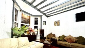 A living room with a beige sofa, a green sofa with cushions, a wooden coffee table, and a red carpet. There is a large window with a view of the outside, a fireplace, and a flat-screen TV mounted on the wall. - Blackpool Central Hotel (Blackpool)