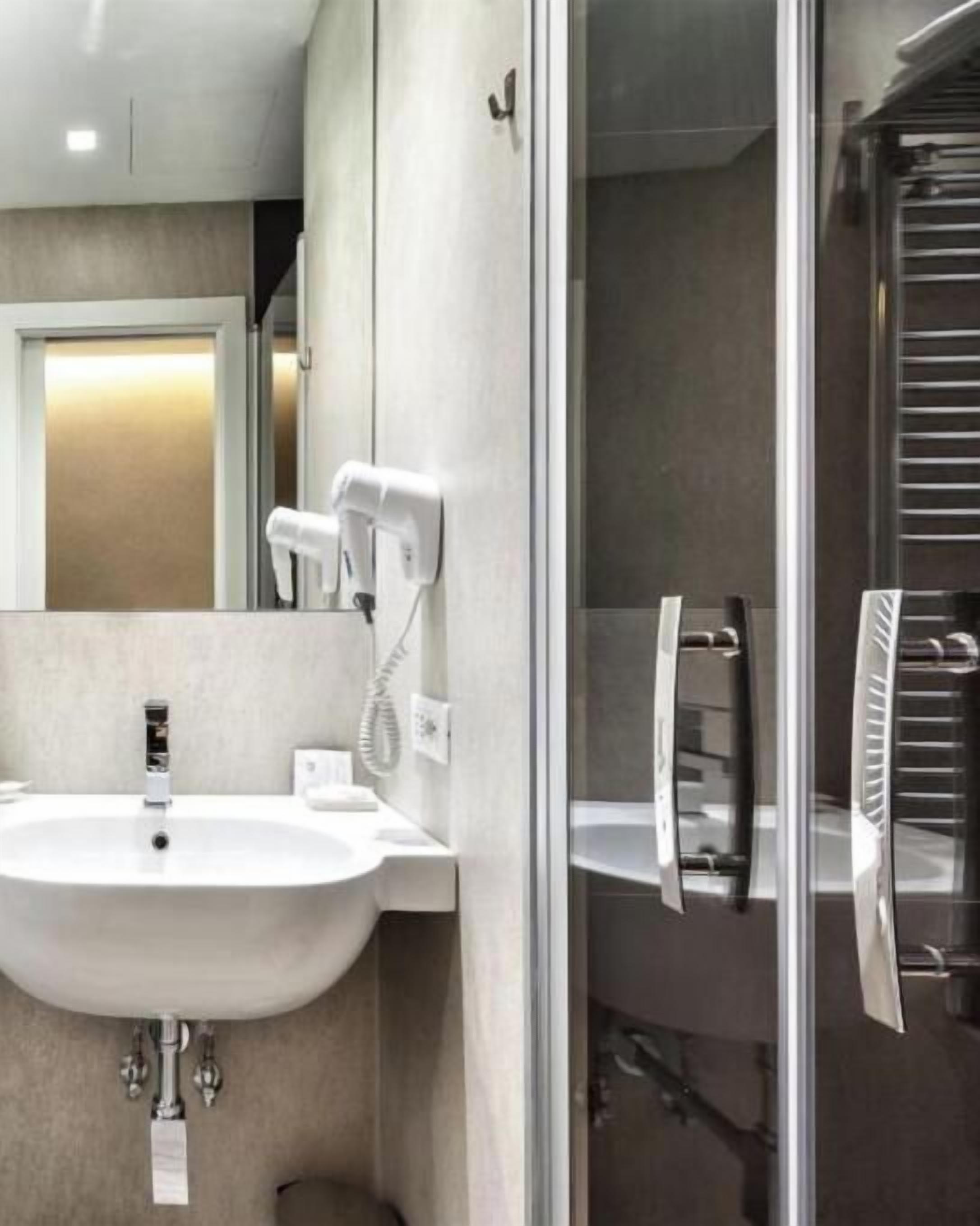A modern bathroom with a white sink, a glass shower enclosure, and a towel rack.