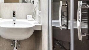 Un baño moderno con un lavabo blanco, una cabina de ducha con paredes de vidrio y un perchero para toallas.