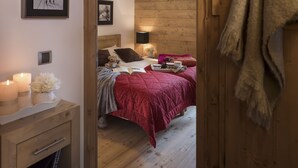A cozy bedroom with a wooden headboard, a bed with a red blanket, a bedside table with candles, and a framed picture on the wall. - CGH Résidence & Spa le Jhana (Tignes)
