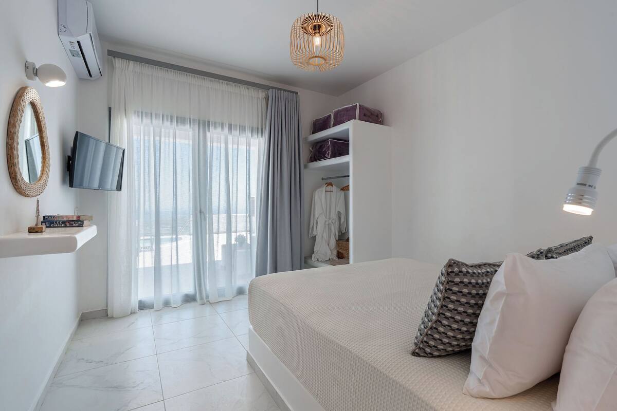 A bedroom with a bed, a TV, a wardrobe, and a window with curtains.