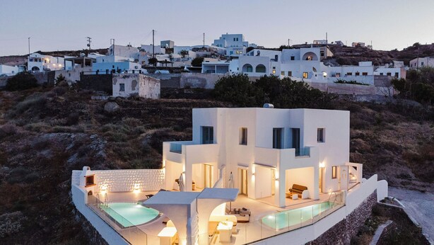 A modern white villa with a swimming pool, stone walls, and a view of a coastal village. - Dream Villa (Santorini)