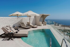 A poolside area with lounge chairs, umbrellas, and a clear view of the ocean.