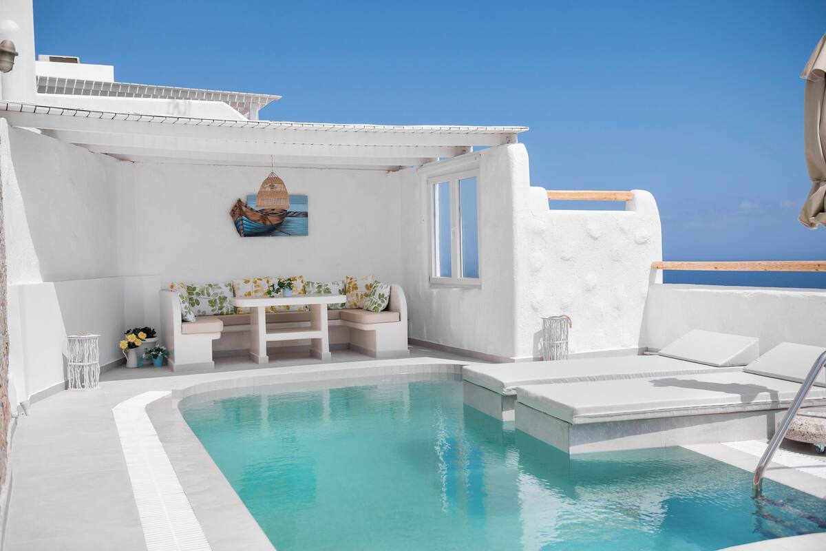 A poolside area with a seating arrangement, a small table with flowers, and a view of the sea.
