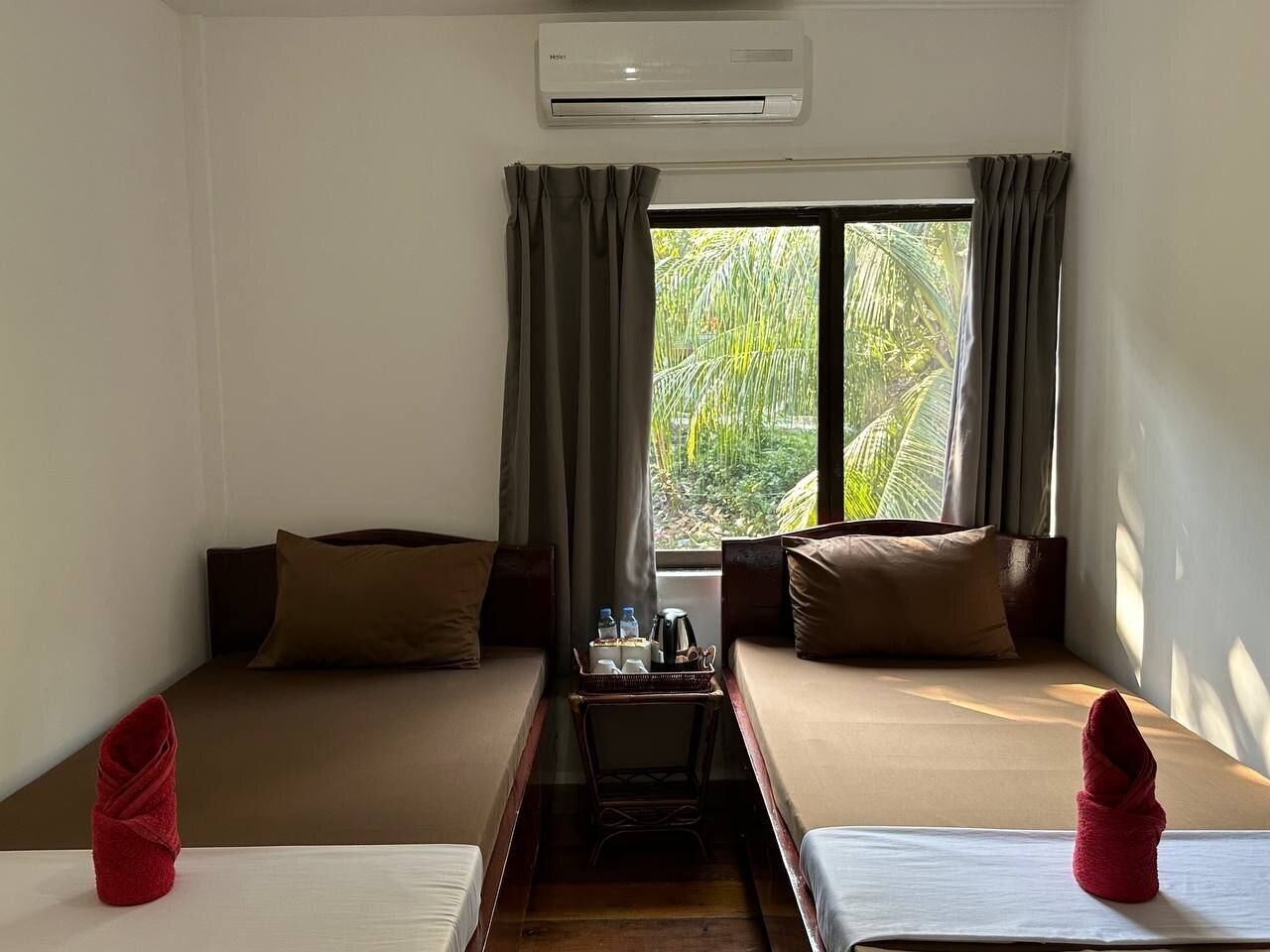 A room with two beds, a small table with a tray of items, and a window with curtains.