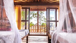 A room with two beds, a wooden ceiling, and large windows overlooking a balcony with a view of trees and a clear sky. - Happy Elephant Bungalows (Koh Rong)