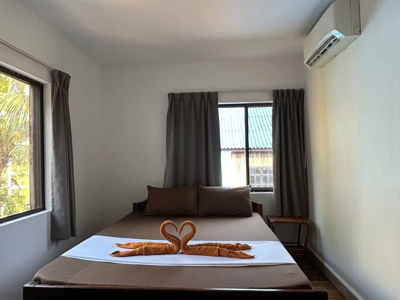 A hotel room with a bed, a window with curtains, an air conditioning unit, and a small table.