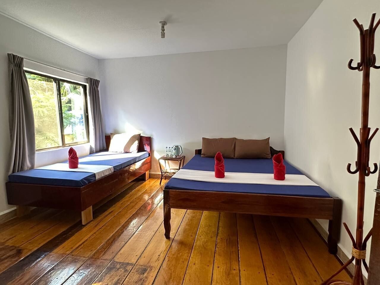 A room with two wooden beds, a wooden floor, a window with curtains, and a coat rack.