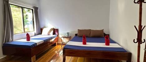 A room with two wooden beds, a wooden floor, a window with curtains, and a coat rack.