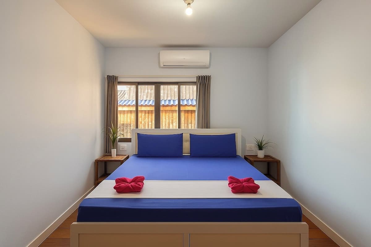 A bedroom with a bed, two nightstands, a window with curtains, an air conditioning unit, and a ceiling light.