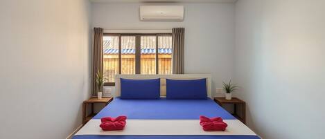 Une chambre à coucher comprenant un lit, deux tables de chevet, une fenêtre avec des rideaux, un appareil de climatisation et un luminaire au plafond.