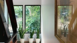 A room with a wooden floor, a large window with a view of greenery, and a framed picture on the wall. - Happy Elephant Bungalows (Koh Rong)