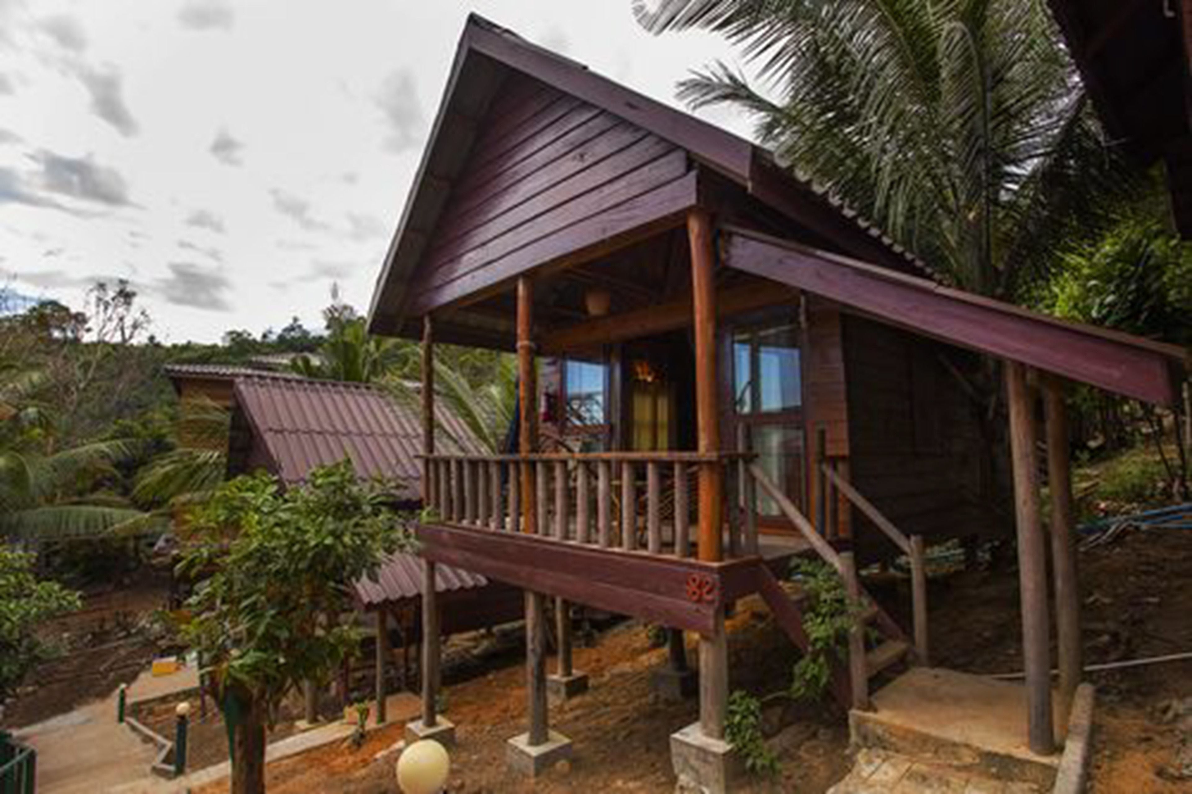A wooden house with a balcony, surrounded by tropical vegetation.