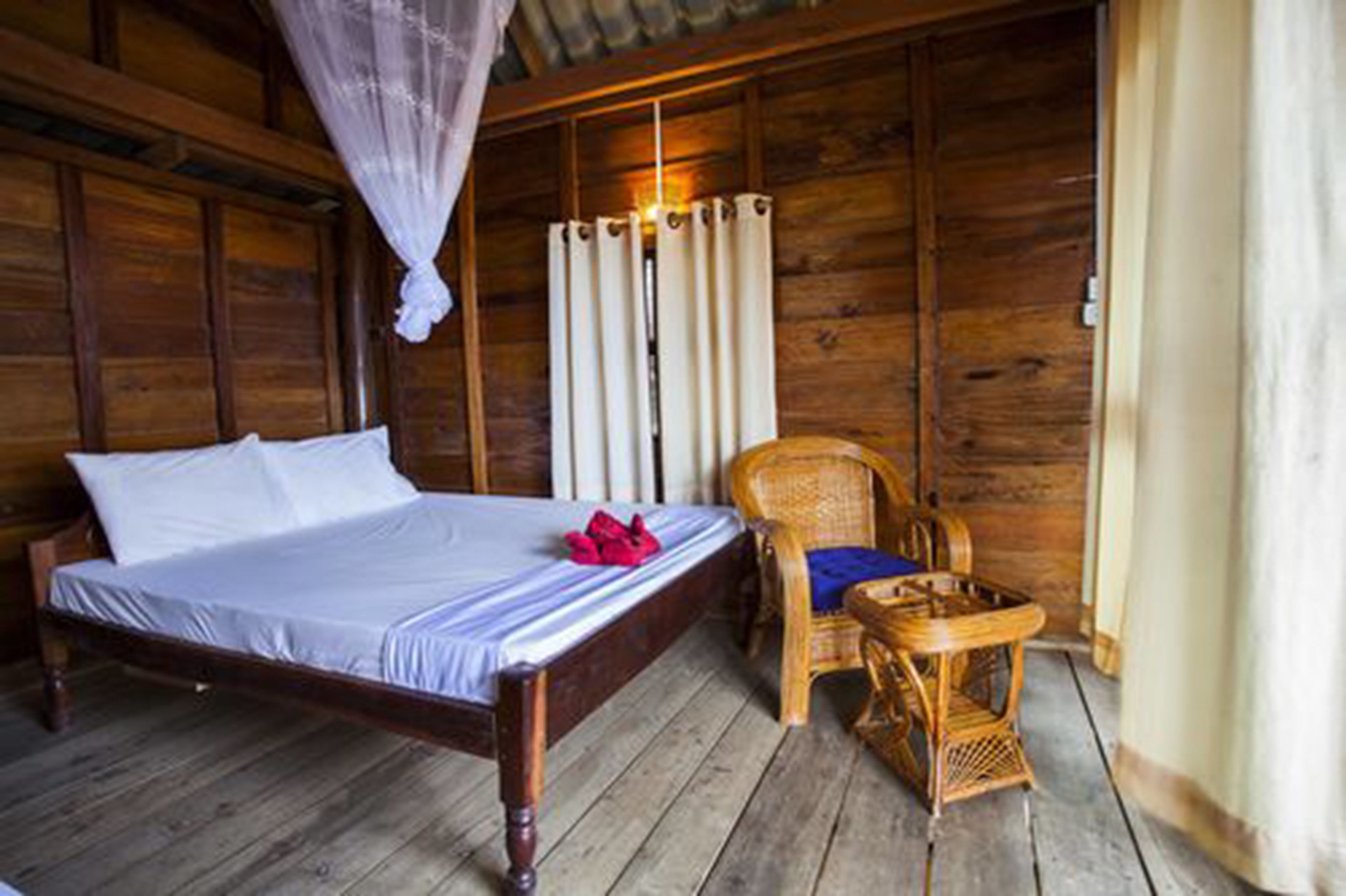 Una habitación de madera con una cama, una silla y una cortina.