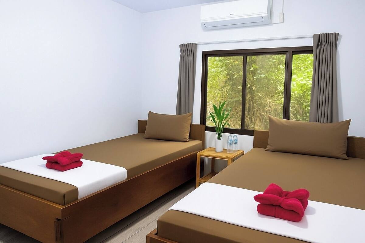 A hotel room with two beds, a small table with a plant, and a window with curtains.