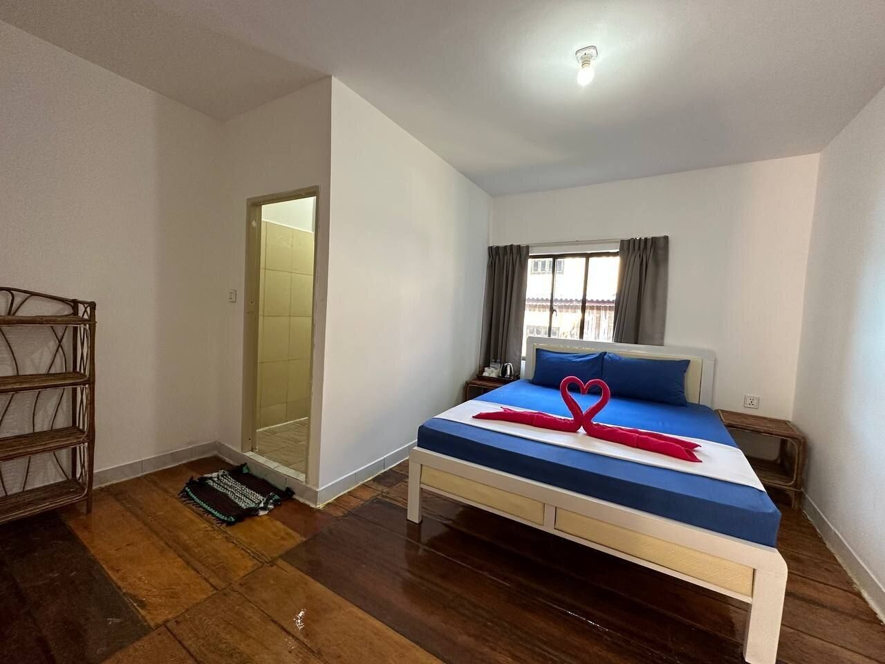 A bedroom with a bed, a wooden floor, a wardrobe, and a window with curtains.