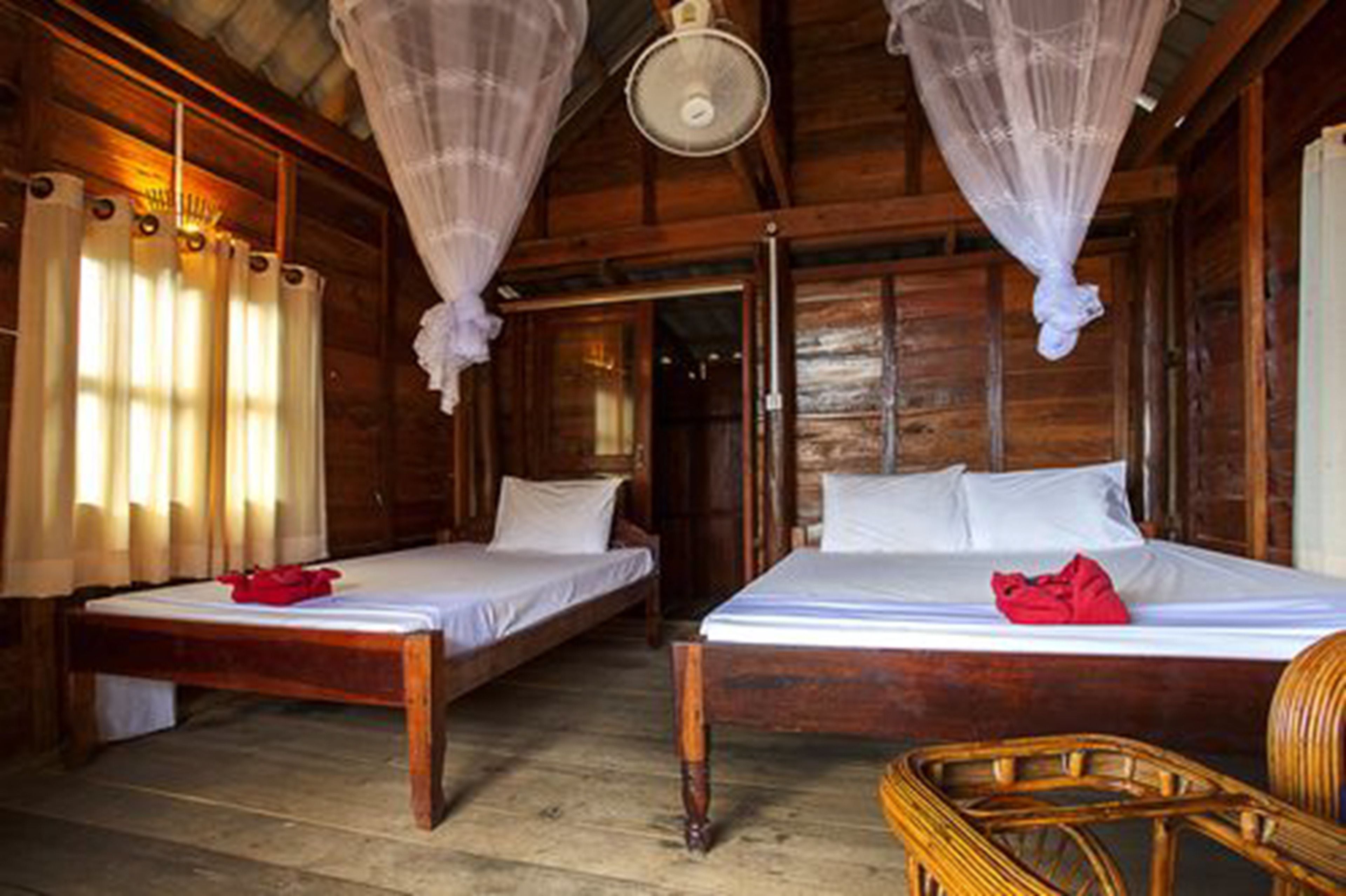 A wooden room with two beds, a wicker chair, and a ceiling fan.