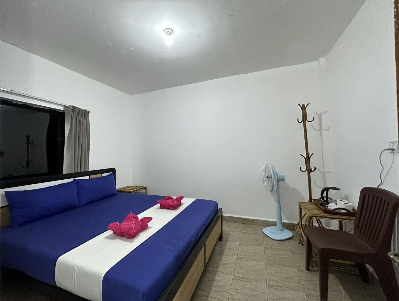 Quarto com cama, cadeira, escrivaninha, cabideiro e ventoinha.