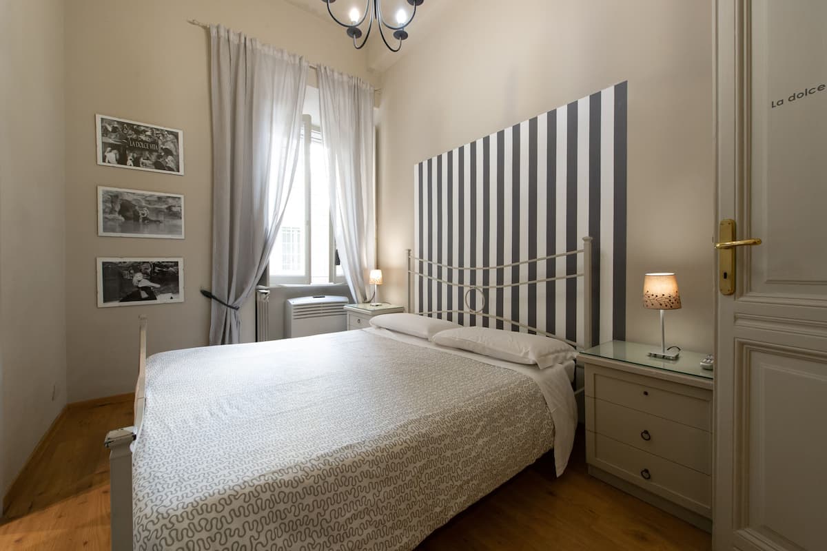 Quarto bem arrumado com cama, mesas de cabeceira, abajur e cabeceira listrada.