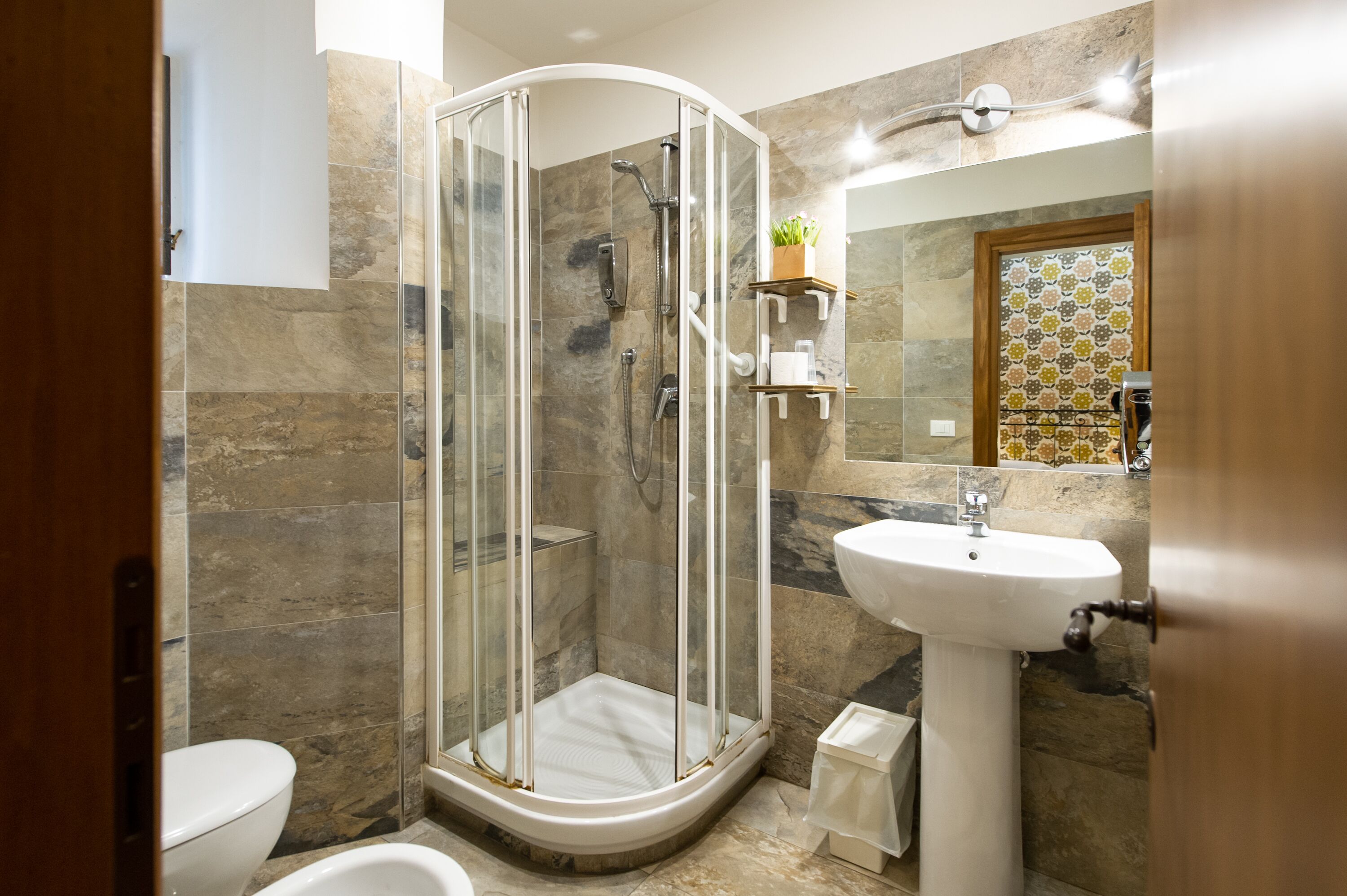 A modern bathroom with a glass-enclosed shower, a pedestal sink, and a toilet.