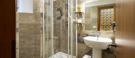 A modern bathroom with a glass-enclosed shower, a pedestal sink, and a toilet.