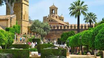 A historic building with a bell tower, surrounded by well-maintained gardens and palm trees.