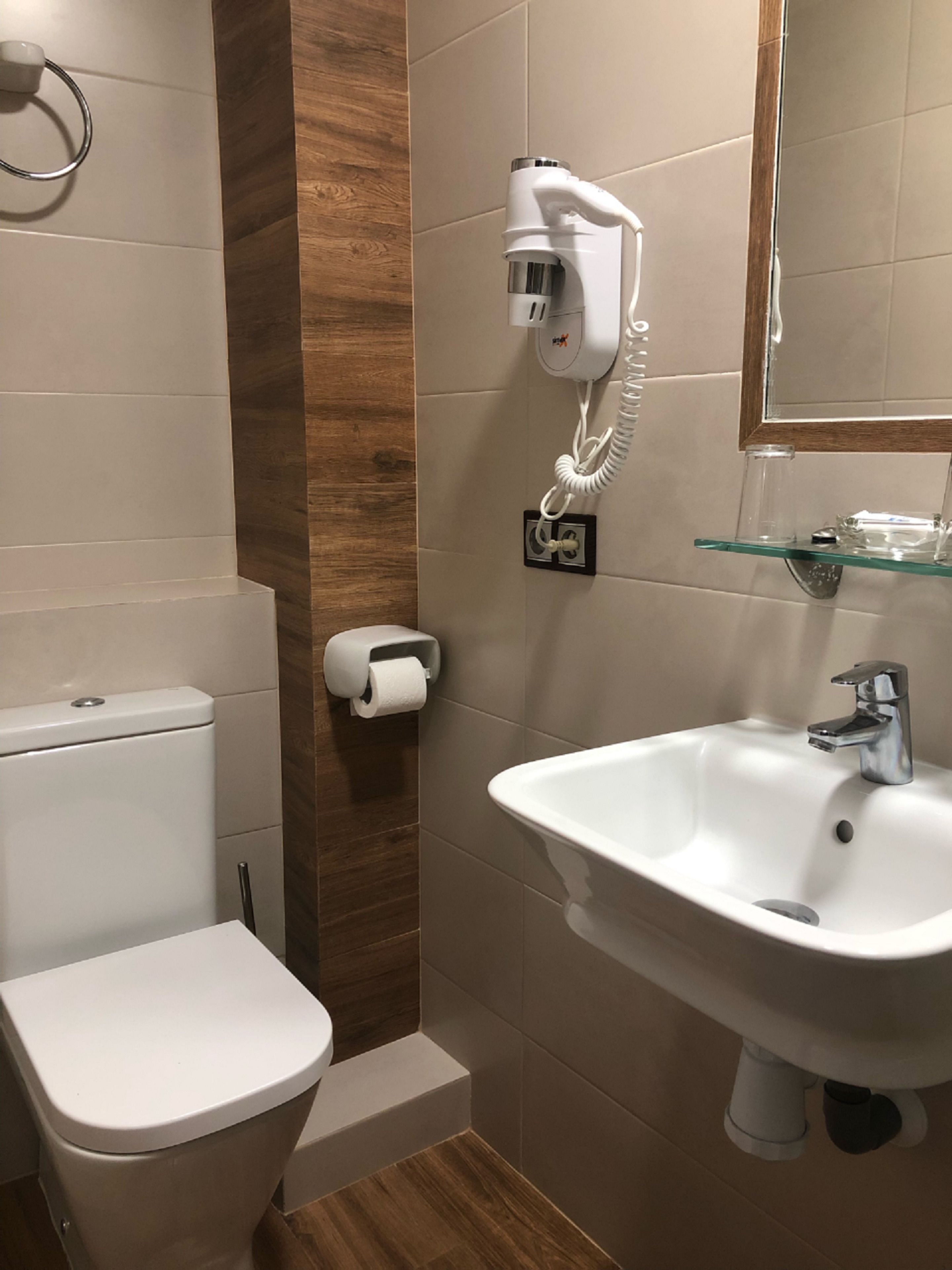 Un baño moderno con inodoro, lavamanos y un secador de pelo montado en la pared.