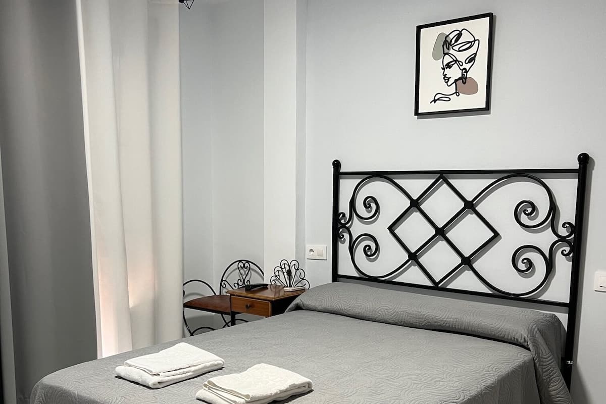 A neatly made bed with a grey bedspread and two folded white towels.