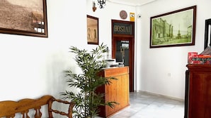 Un'area di accoglienza con una panca di legno, una pianta in vaso, uno sportello della reception e quadri appesi alle pareti.