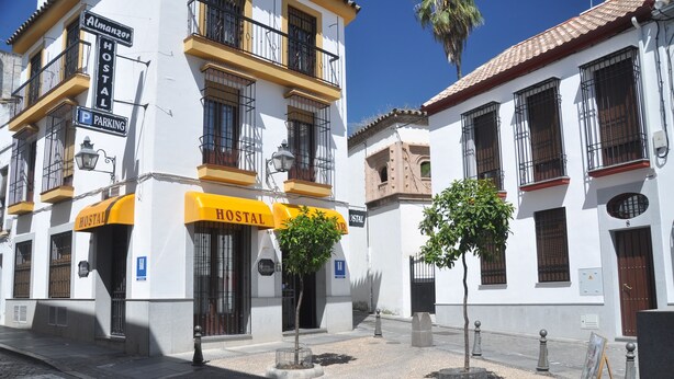 Un edificio bianco con un cartello giallo che indica un ostello, un segnale di parcheggio e un piccolo albero di fronte.