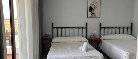 A bedroom with two beds, a window with curtains, a painting on the wall, and a small table with a lamp.