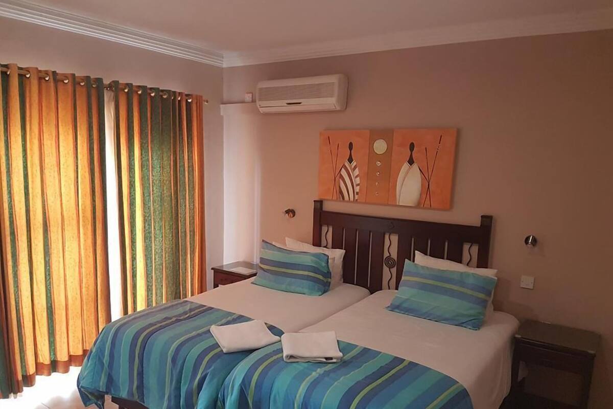 A hotel room with a bed, two bedside tables, an air conditioning unit, and curtains.