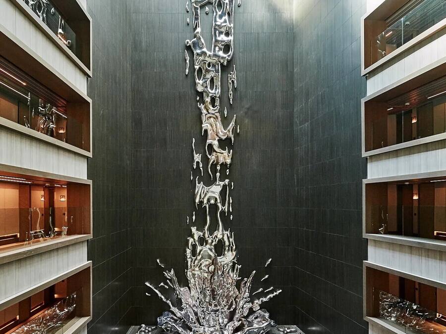 Un interior moderno con una escultura metálica central que recuerda a una cascada, rodeada de estantes con diversos objetos.