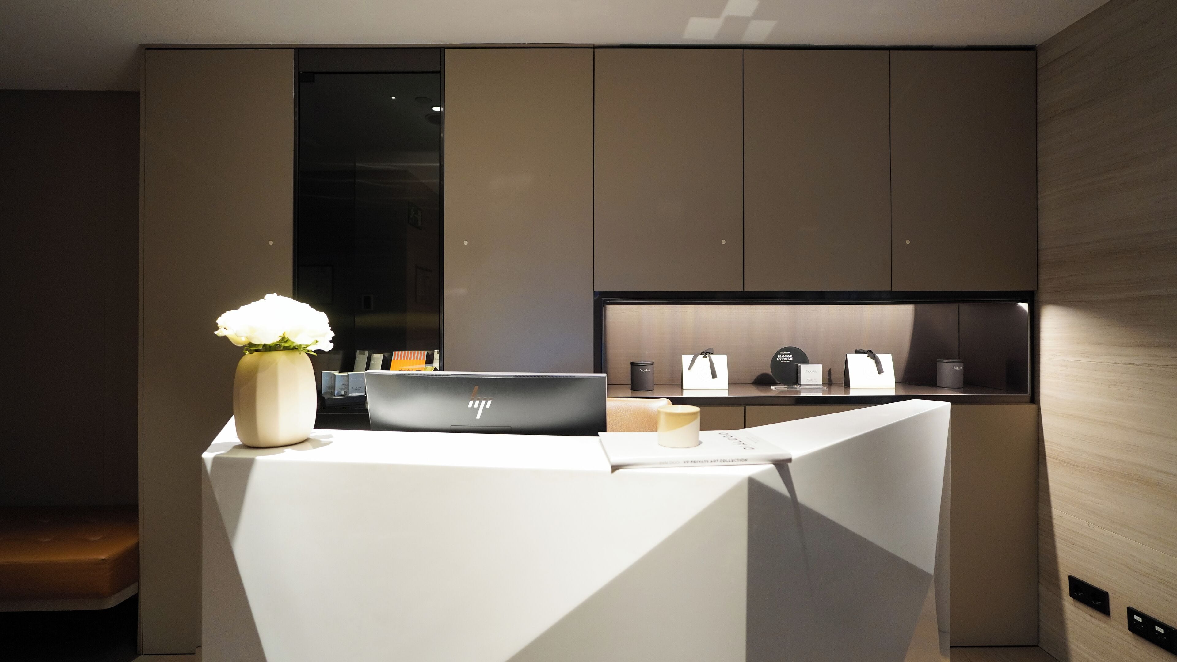 A modern kitchen with a white countertop, a vase with white flowers, and a laptop.