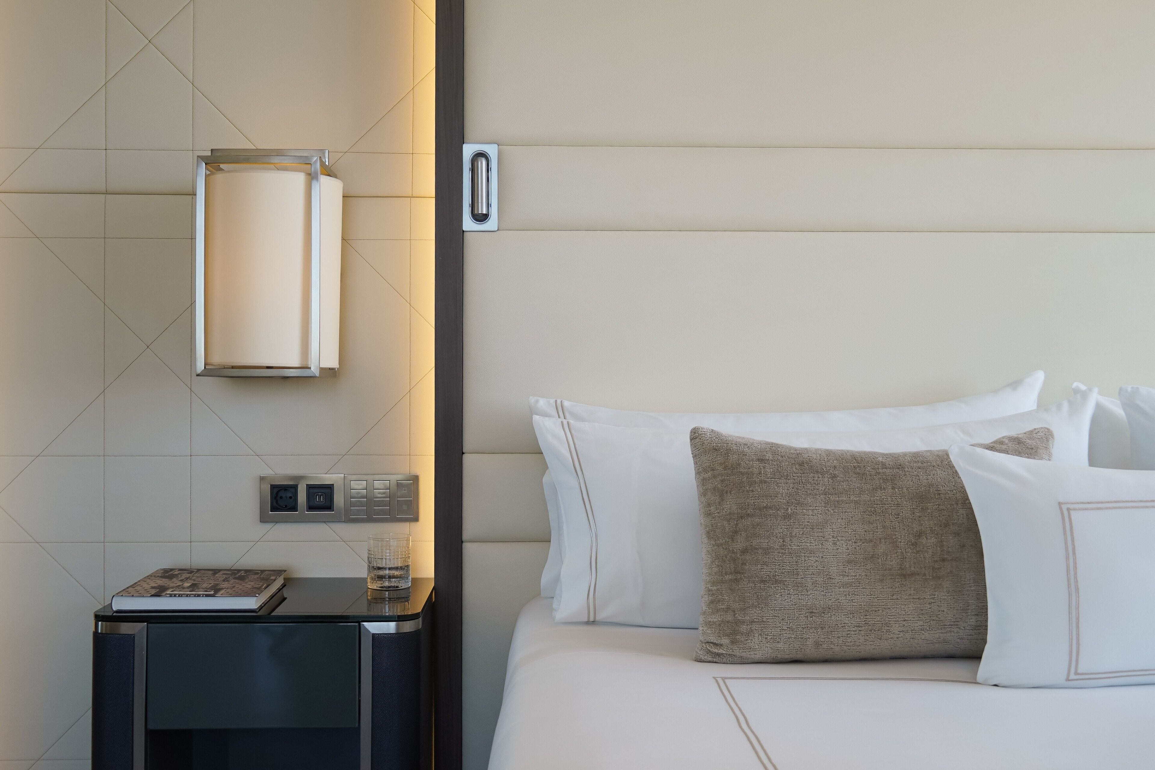Habitación de hotel impecable con cama, mesita de noche y lámpara de pared.
