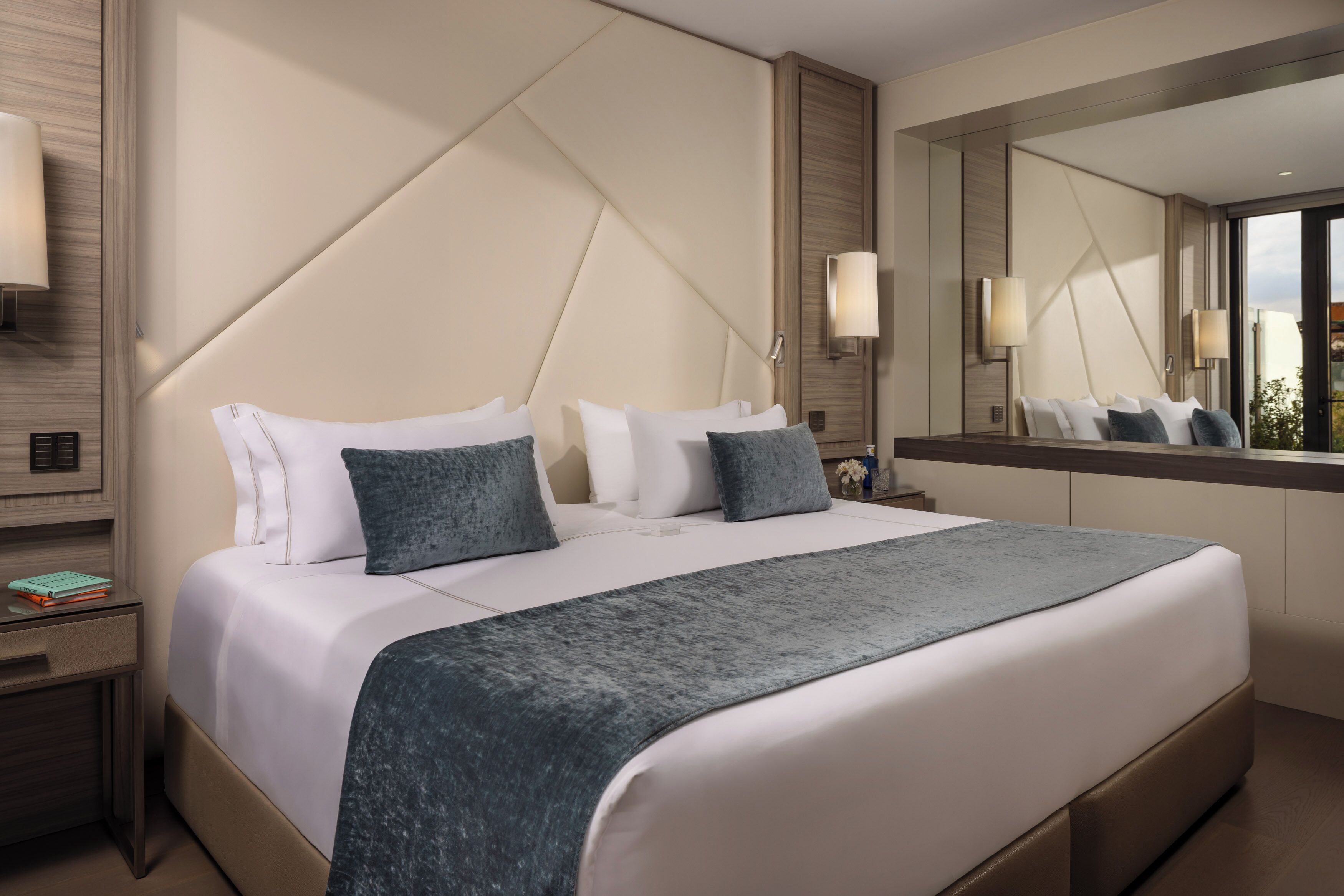Een moderne hotelkamer met een groot bed, een nachtkastje, een grote spiegel en uitzicht op de stad.