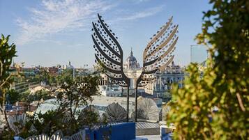 Una escultura de metal con diseños de hojas, una zona de estar azul y vistas de un paisaje urbano con edificios y una estructura en forma de cúpula.