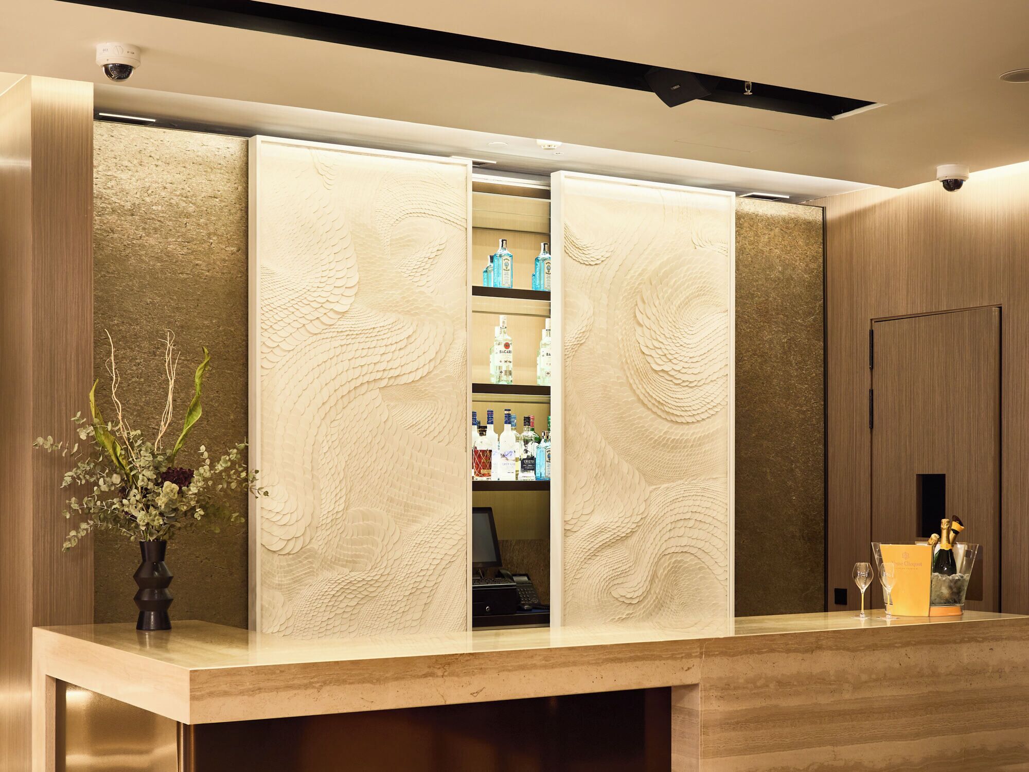 Un área de recepción con un mostrador de madera, un jarrón con flores y una mini-bar con varias botellas.