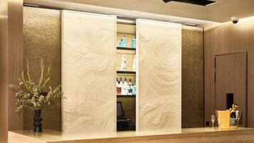 Un área de recepción con un mostrador de madera, un jarrón con flores y una mini-bar con varias botellas.